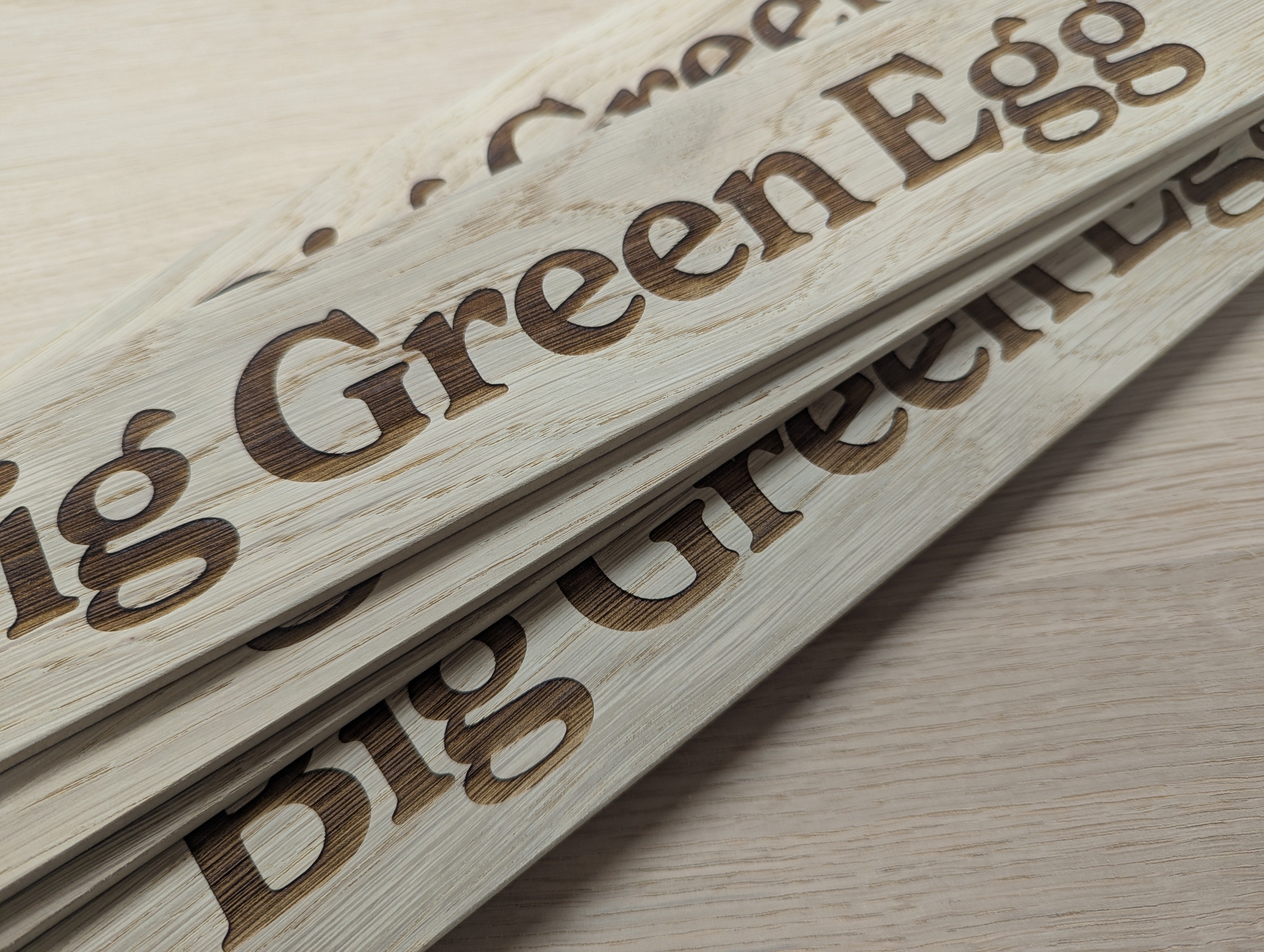 Wooden sign with 'Big Green Egg' branding on a light wooden surface